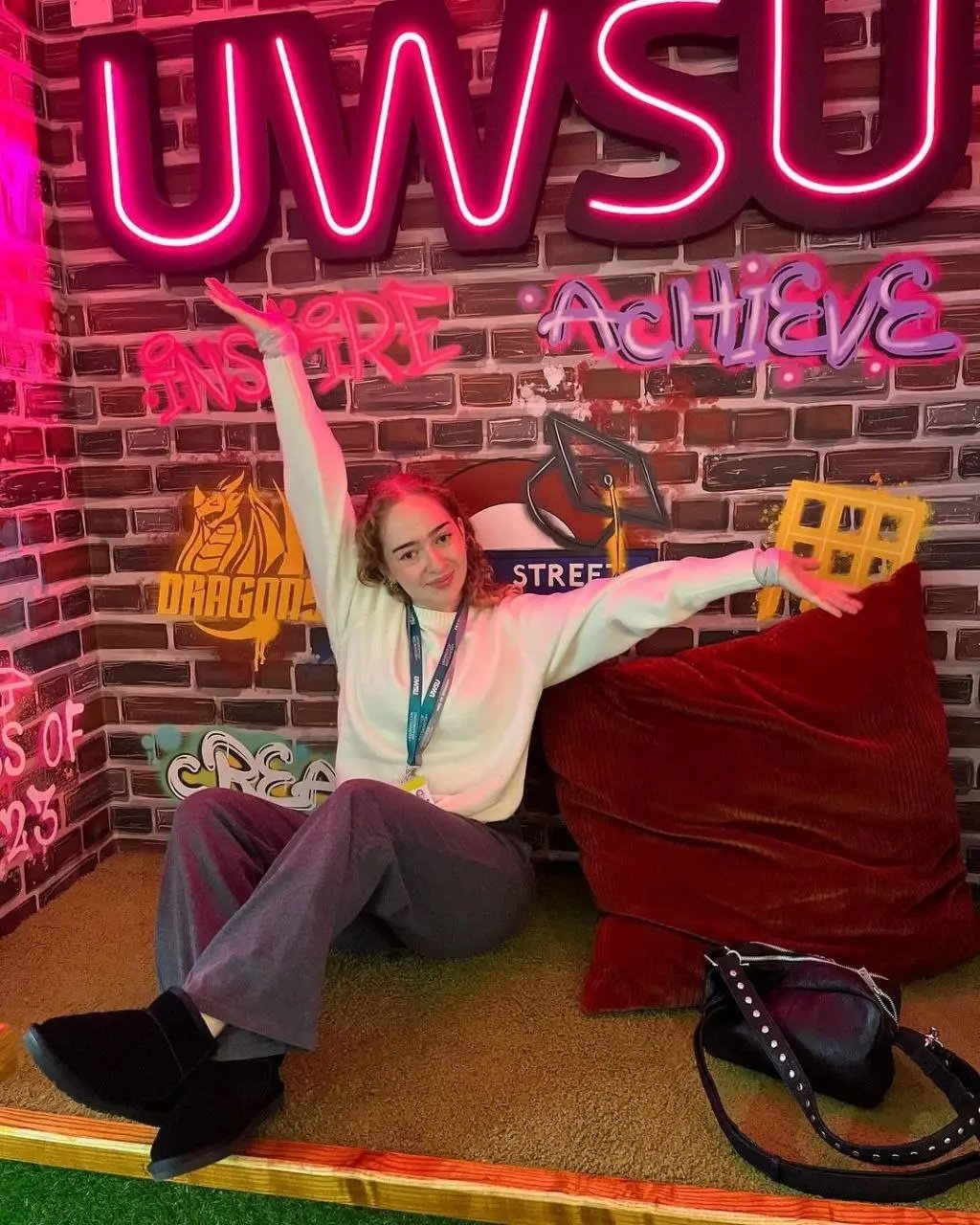 IEC Alumna und Social Media Amabssador Ezo sitzt auf einem Lounge-Sofa vor einer Neon-Wand mit der Aufschrift "UWSU".