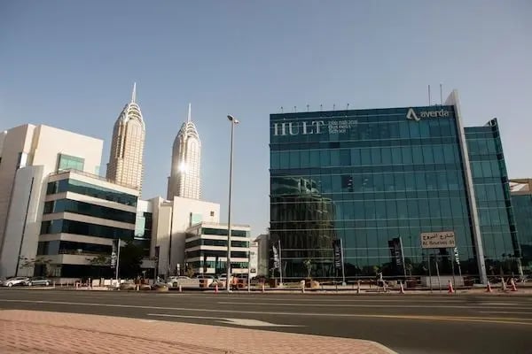 Moderne Glasfassade der Hult International Business School in Dubai mit Skyline im Hintergrund.