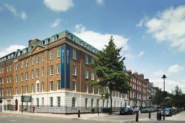 Universitätsgebäude der Hult University an einer Straßenecke in London, umgeben von Bäumen und Laternen bei blauem Himmel.