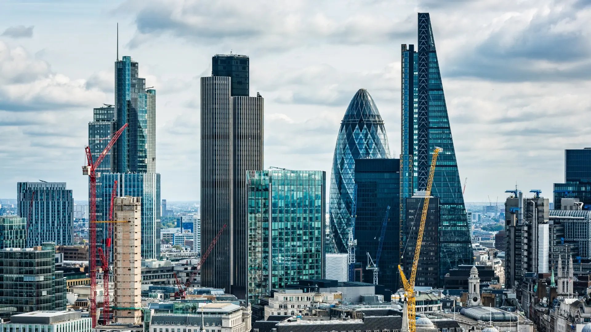 Skyline von London mit modernen Wolkenkratzern, darunter The Gherkin und The Leadenhall Building, sowie Baukränen im Vordergrund.