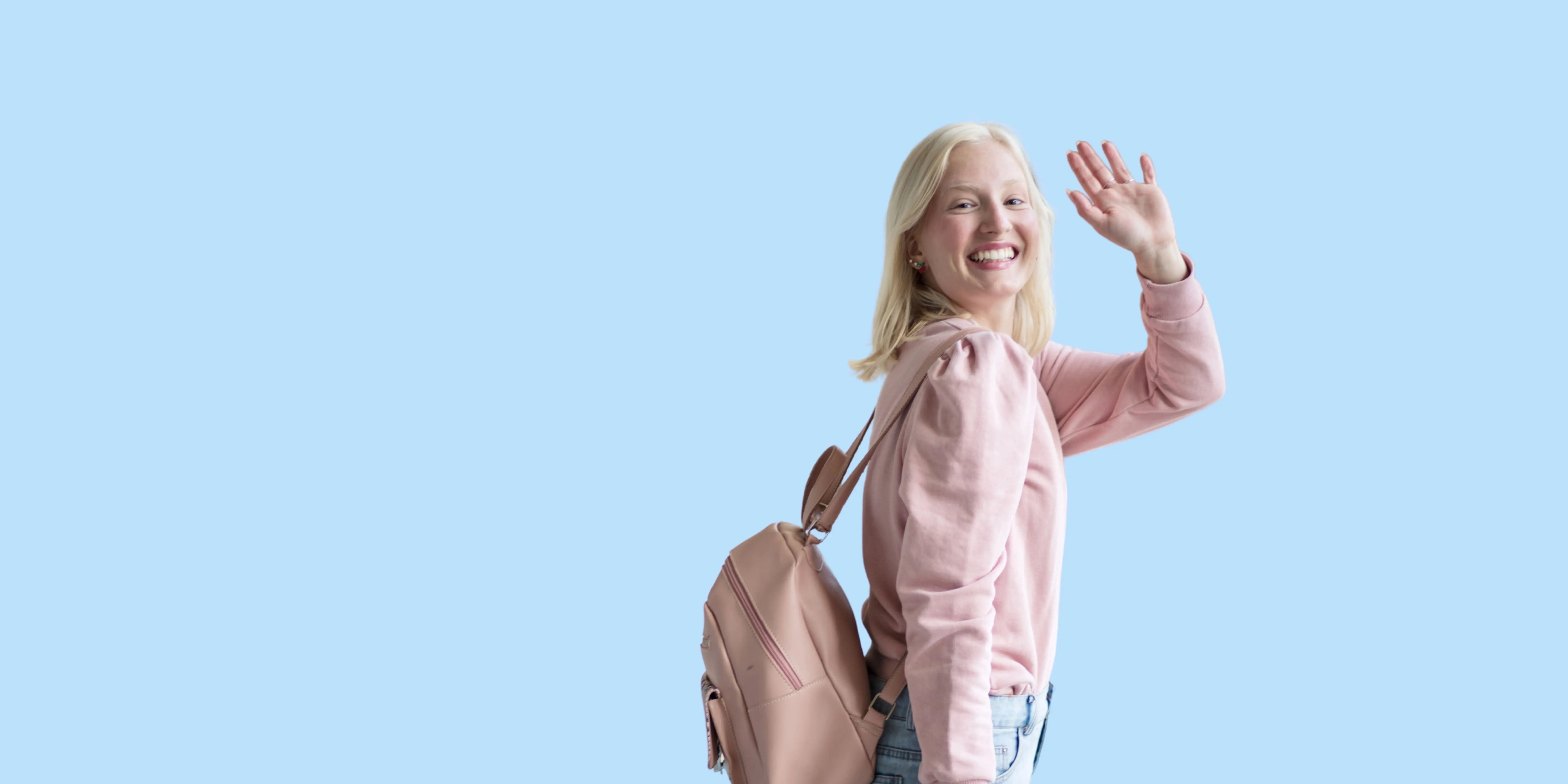 Junge Frau mit blondem Haar lächelt und winkt, symbolisierend einen sorgenfreien Start ins Auslandssemester.