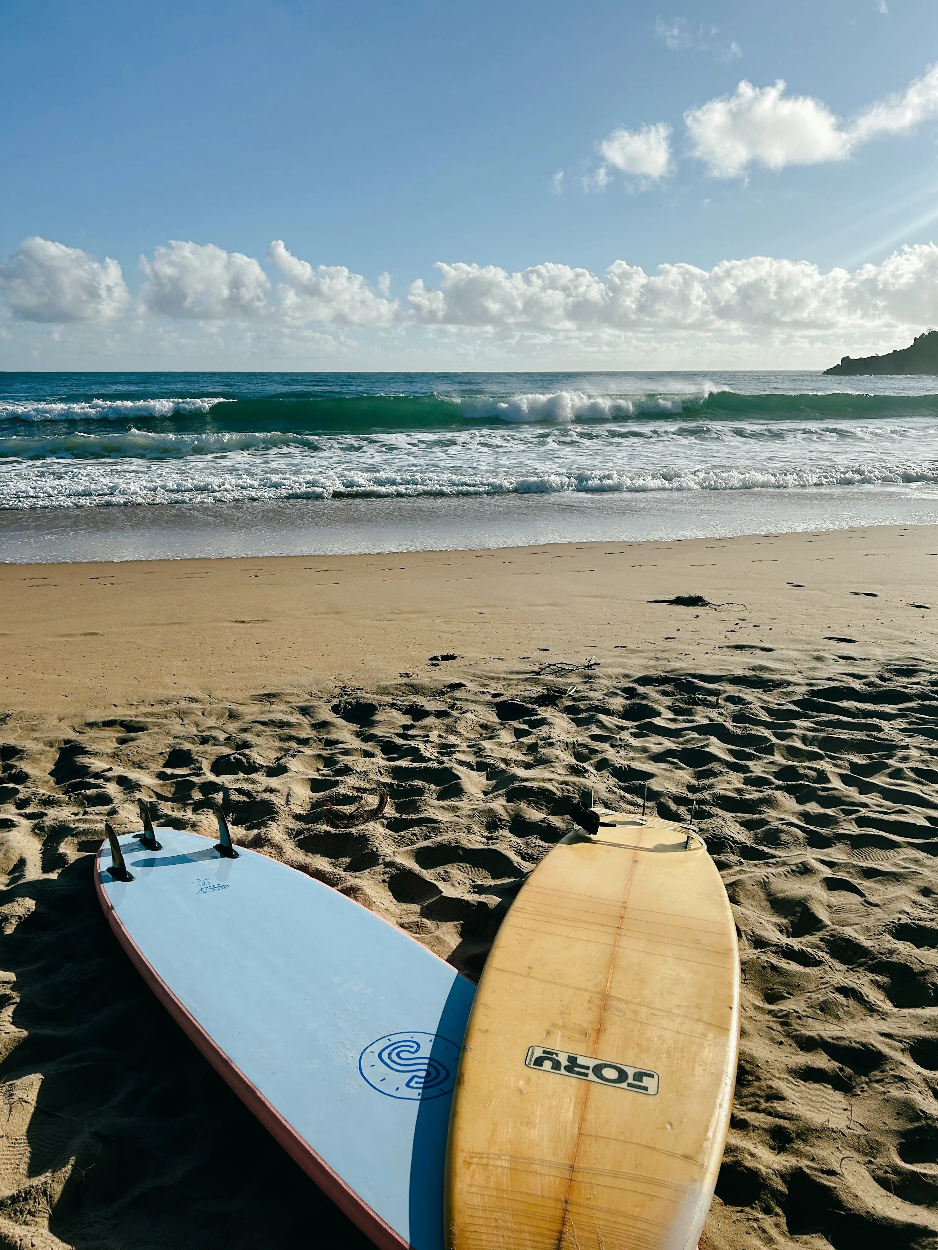 Surfboards liegen am Sandstrand mit Blick auf das Meer und brechende Wellen.