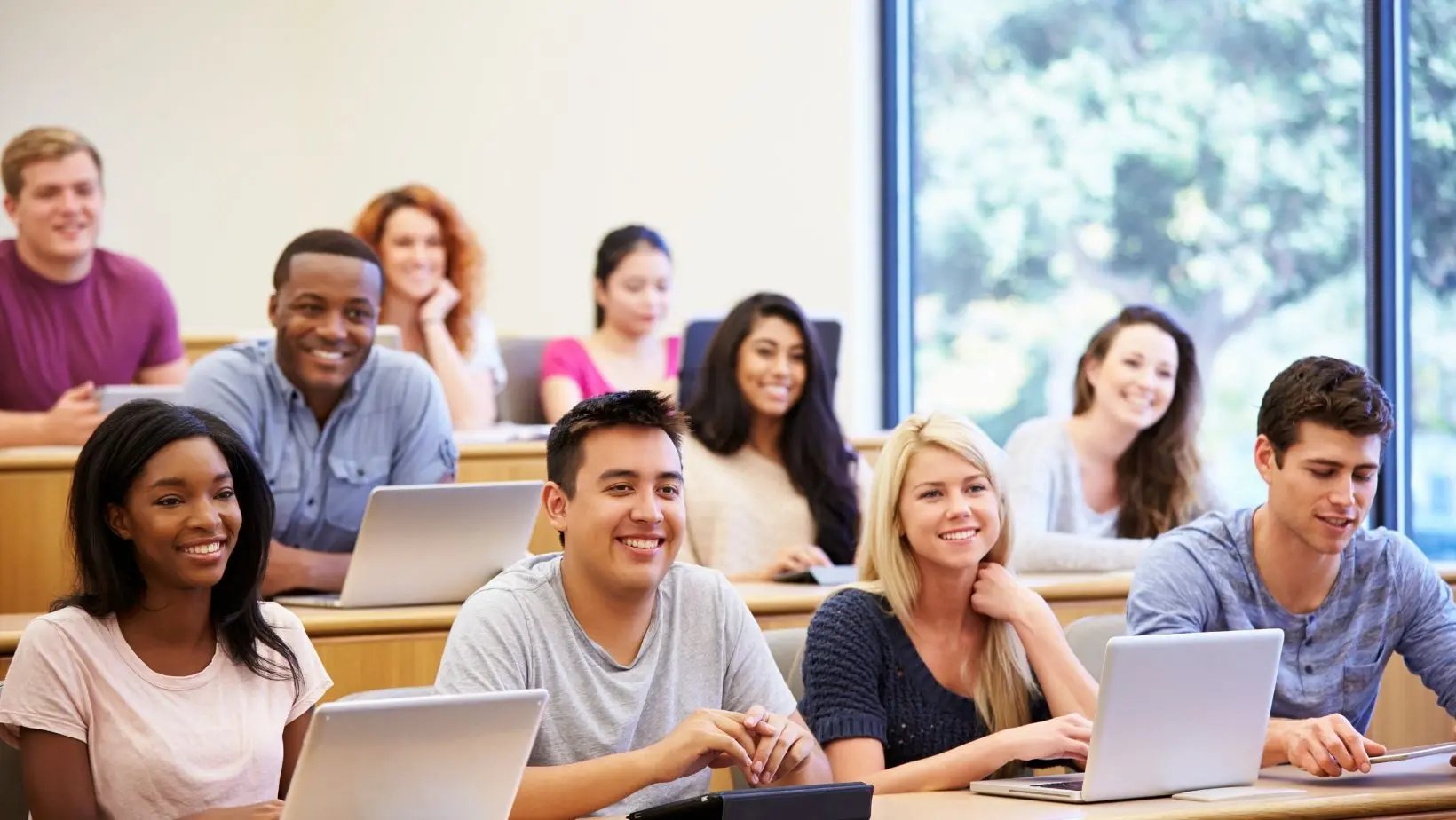 Gruppe lächelnder Studierender mit Laptops im Hörsaal. 