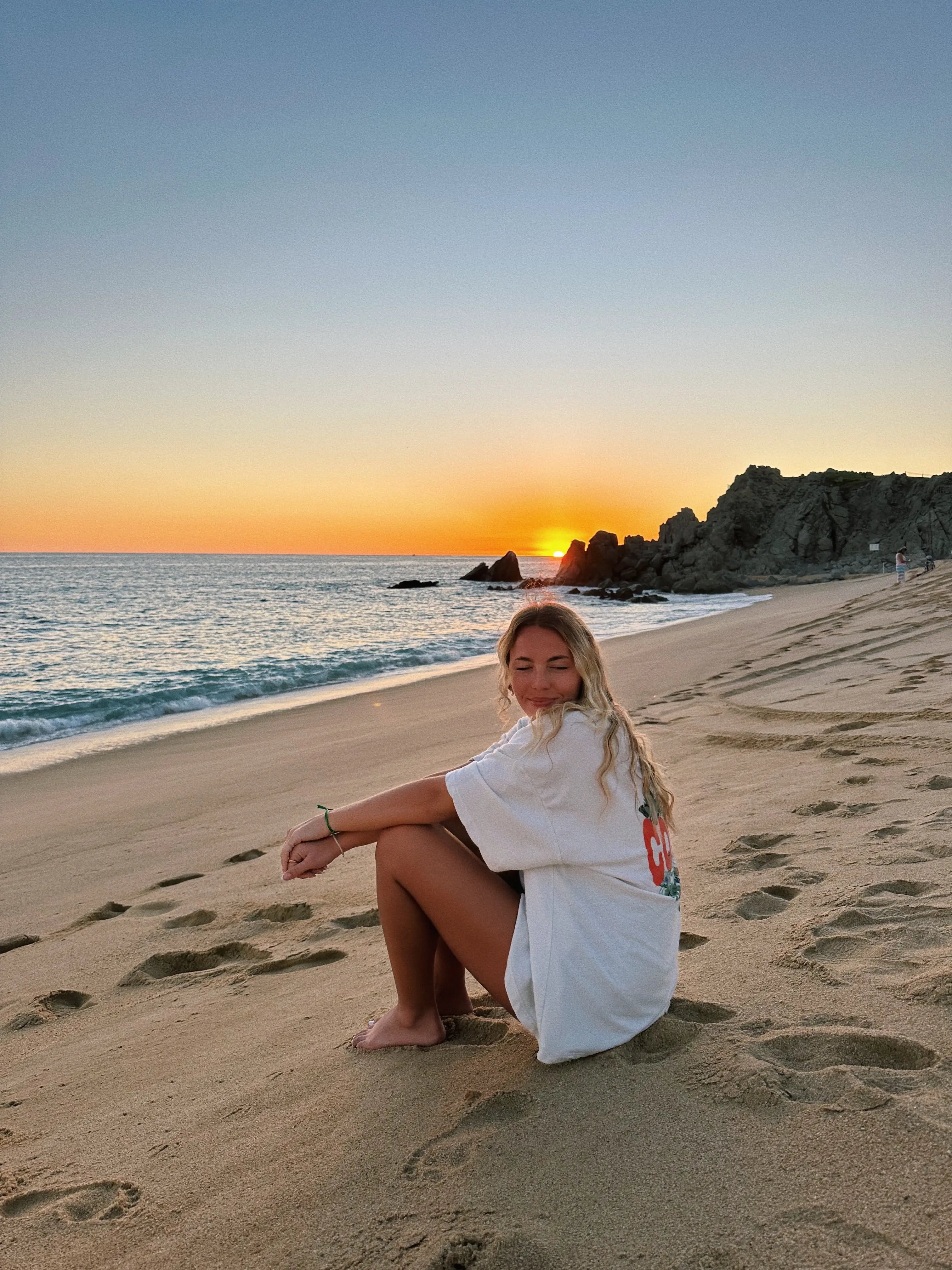 Mädchen sitzt mit geschlossenen Augen am Strand im Sonnenuntergang